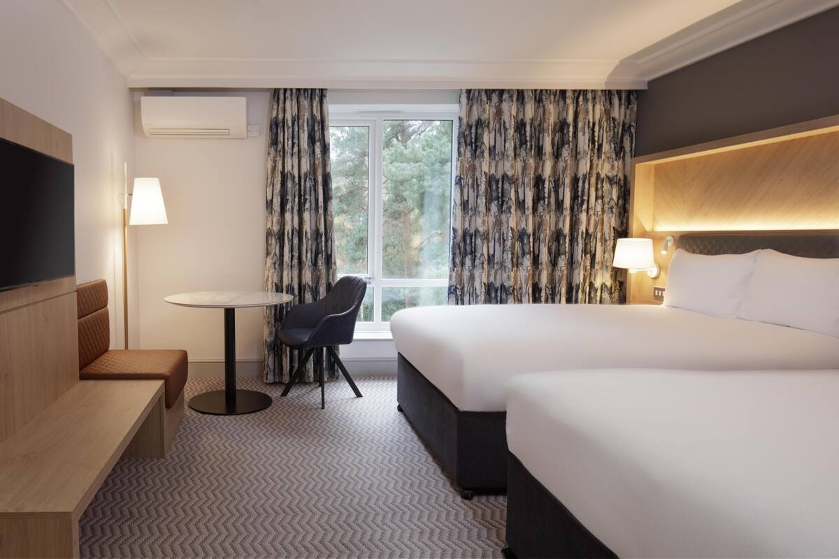 A hotel room with a large bed, a desk, a chair, a TV, and a window with curtains.