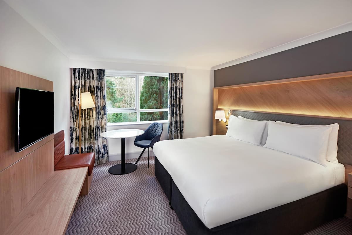A hotel room with a bed, a TV, a small table, a chair, and a window with curtains.