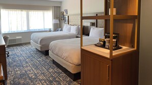 A hotel room with two beds, a desk, a chair, a minibar, and a large window with curtains. - DoubleTree by Hilton Tinton Falls - Eatontown (Tinton Falls)