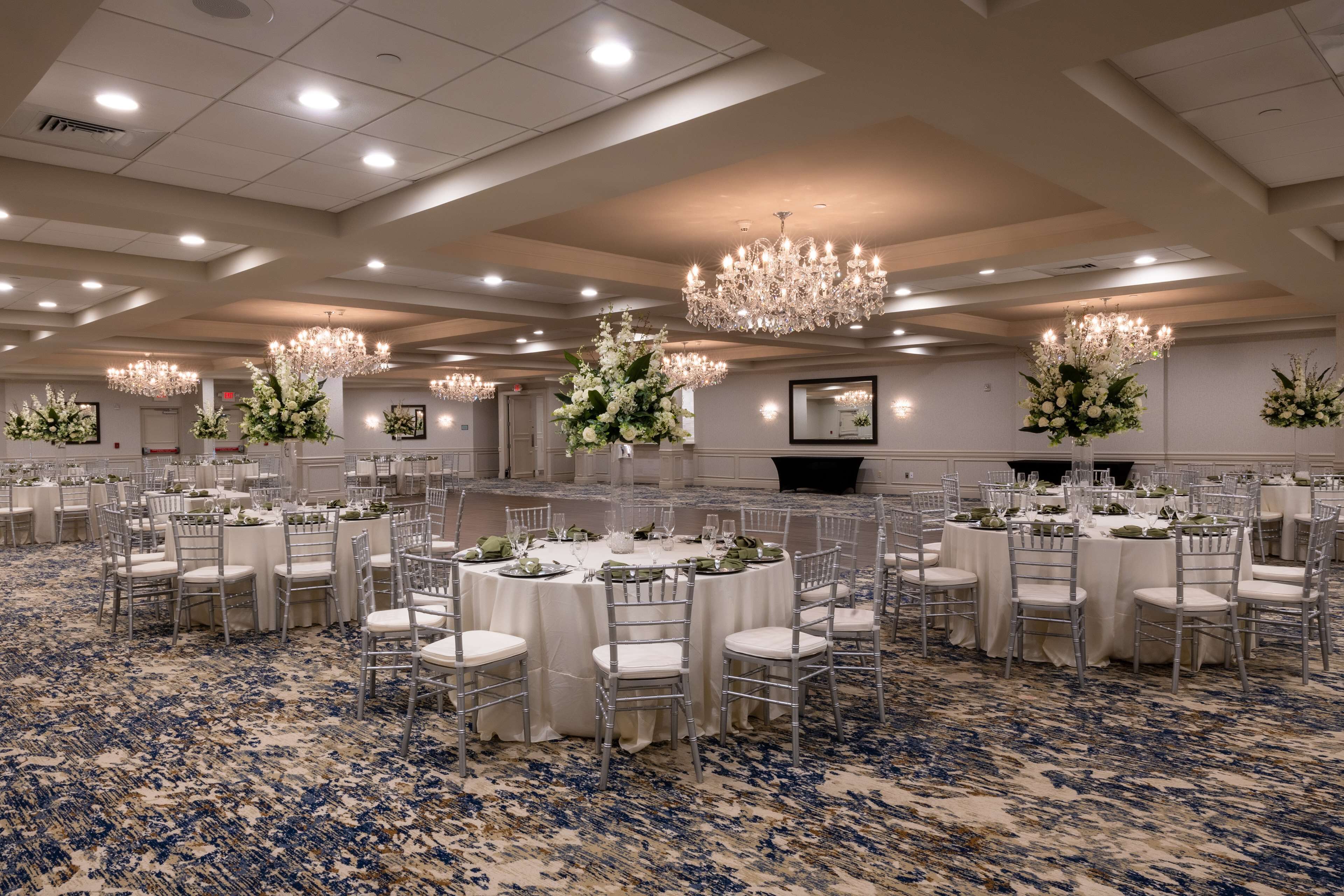 A banquet hall with round tables, white tablecloths, and silver chairs.