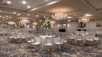 A banquet hall with round tables, white tablecloths, and silver chairs.