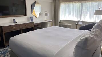 A hotel room with a large bed, a desk with a chair, a television, a mirror, and a window with curtains.