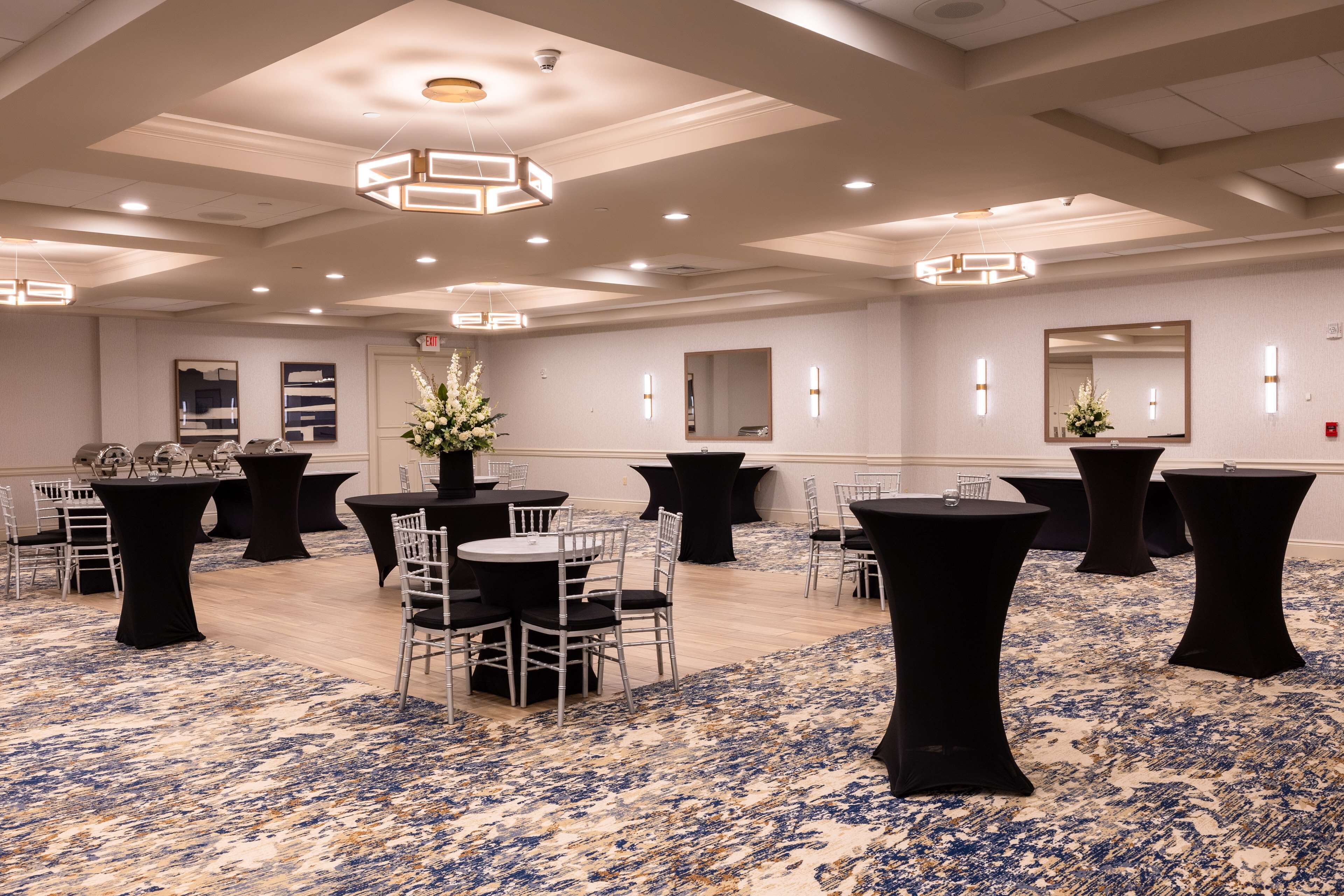 A spacious conference room with round tables, chairs, and black tablecloths.