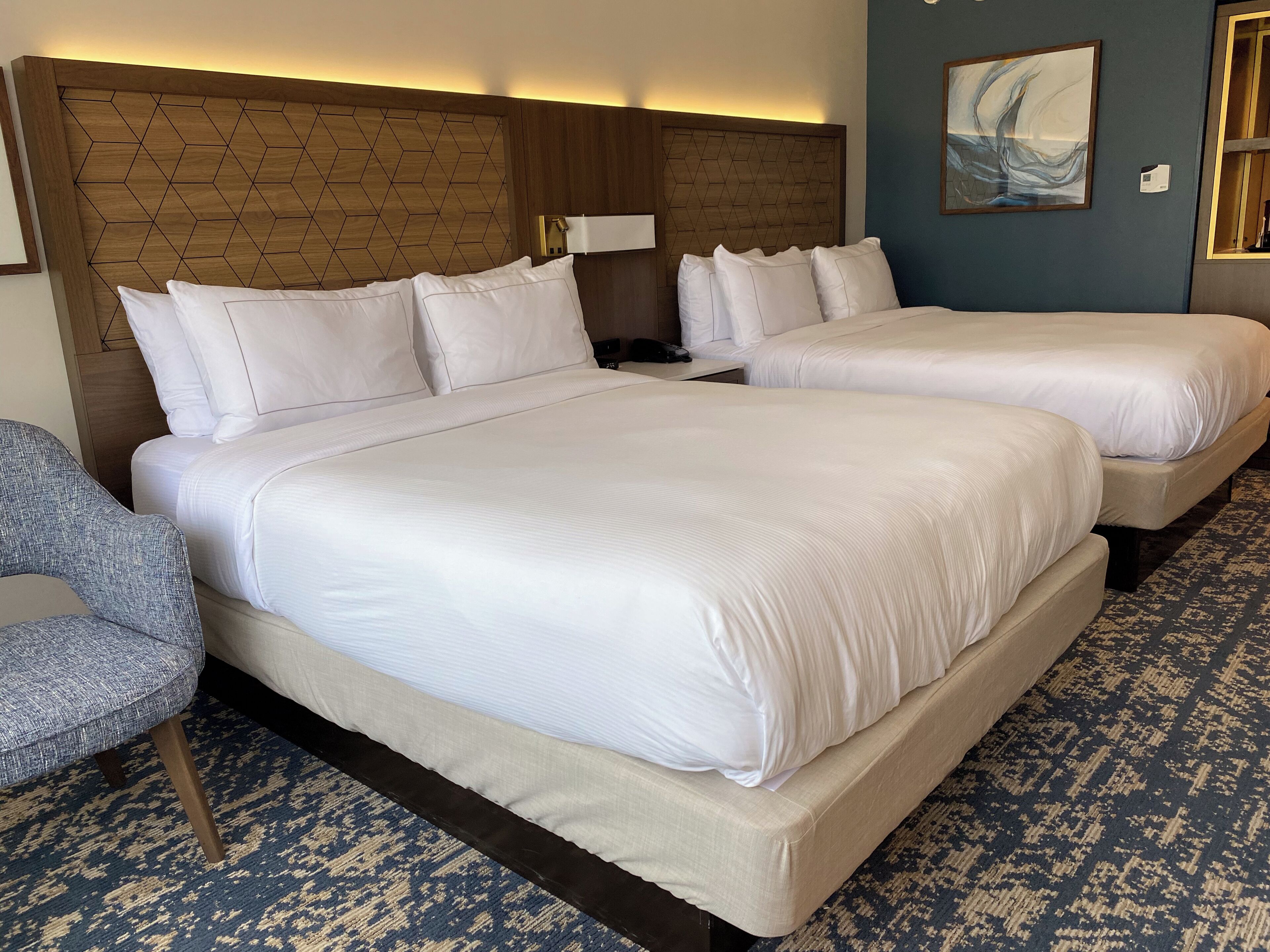 Habitación de hotel con una cama grande, una cama más pequeña, una silla y una alfombra estampada.
