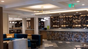 A modern hotel lobby with a blue sofa, a round coffee table, a stone wall with a wood panel design, and a minibar. - DoubleTree by Hilton Tinton Falls - Eatontown (Tinton Falls)