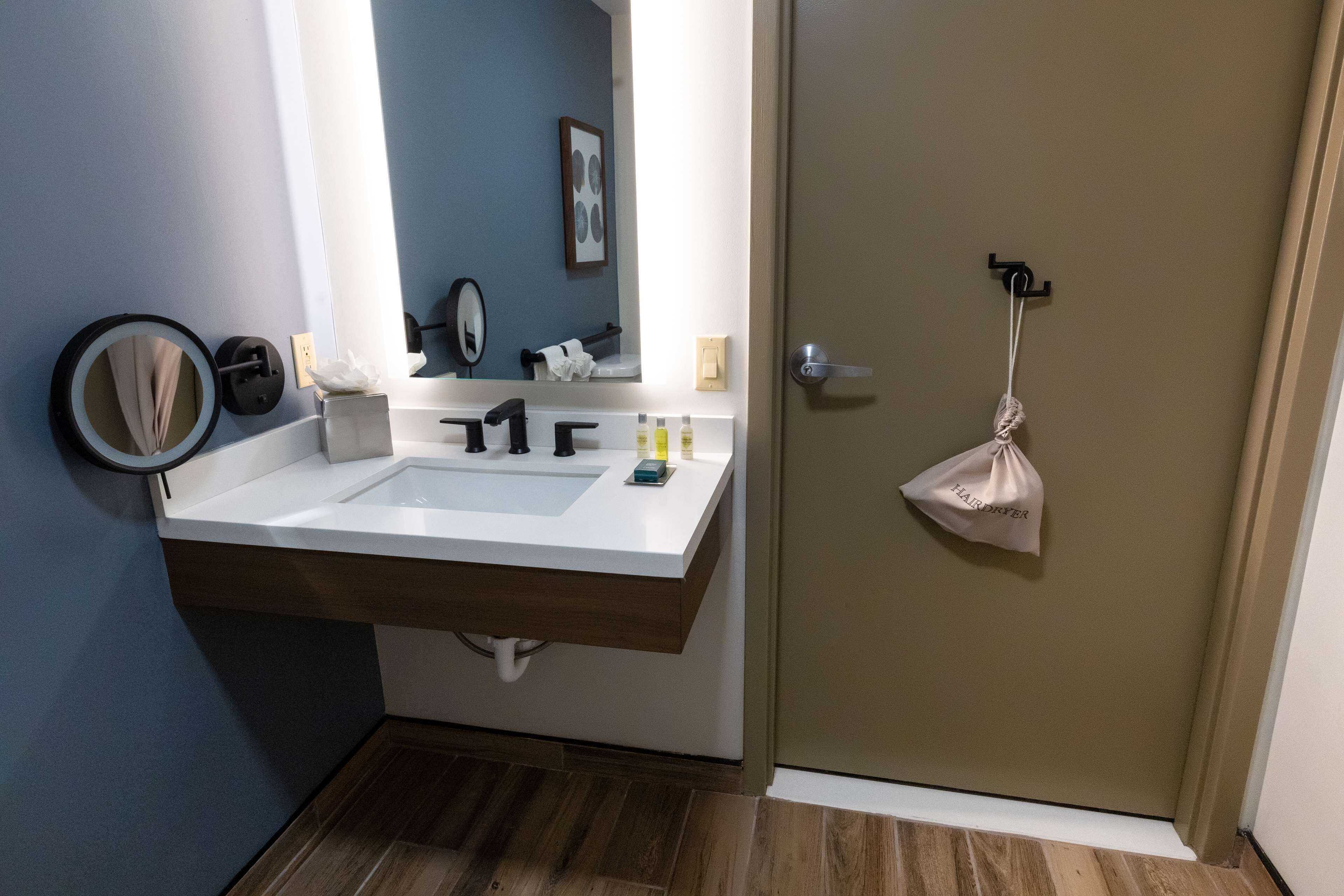 A bathroom with a large sink, mirror, towel rack, and a door with a towel hanging on it.