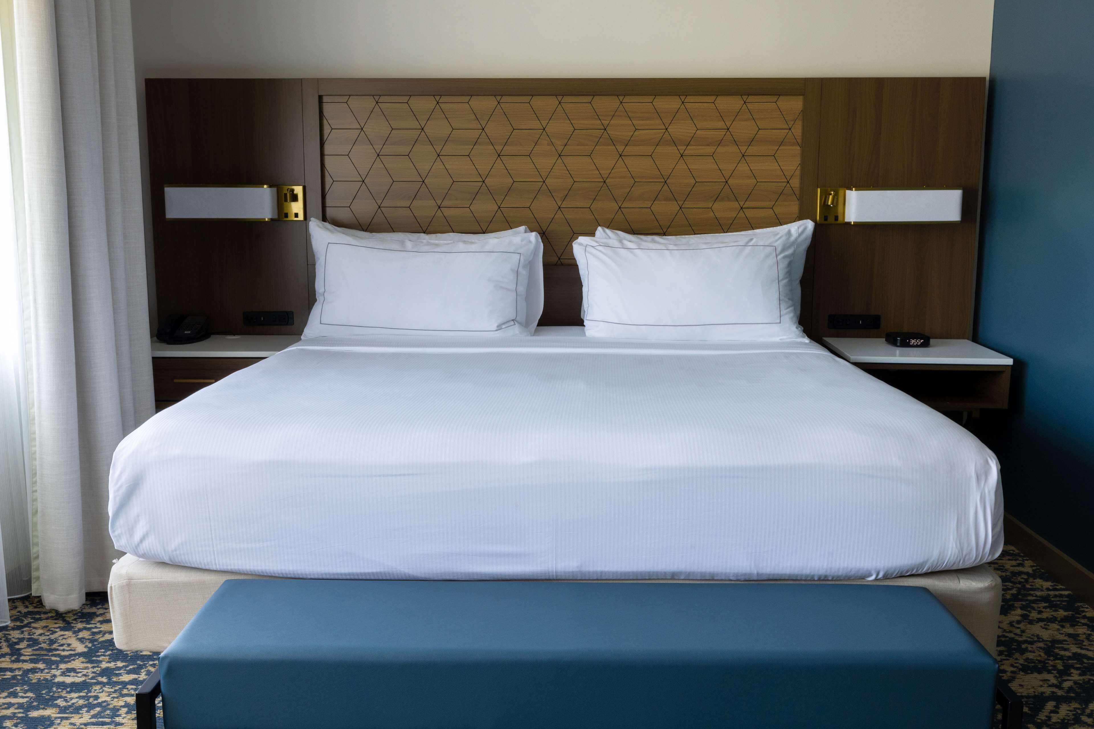 A hotel room with a large bed, two bedside tables, a nightstand, and a bench.