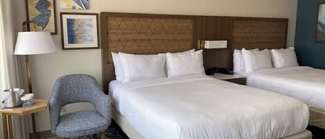 Une chambre d’hôtel avec deux lits, une chaise, une lampe et des œuvres d’art accrochées au mur.