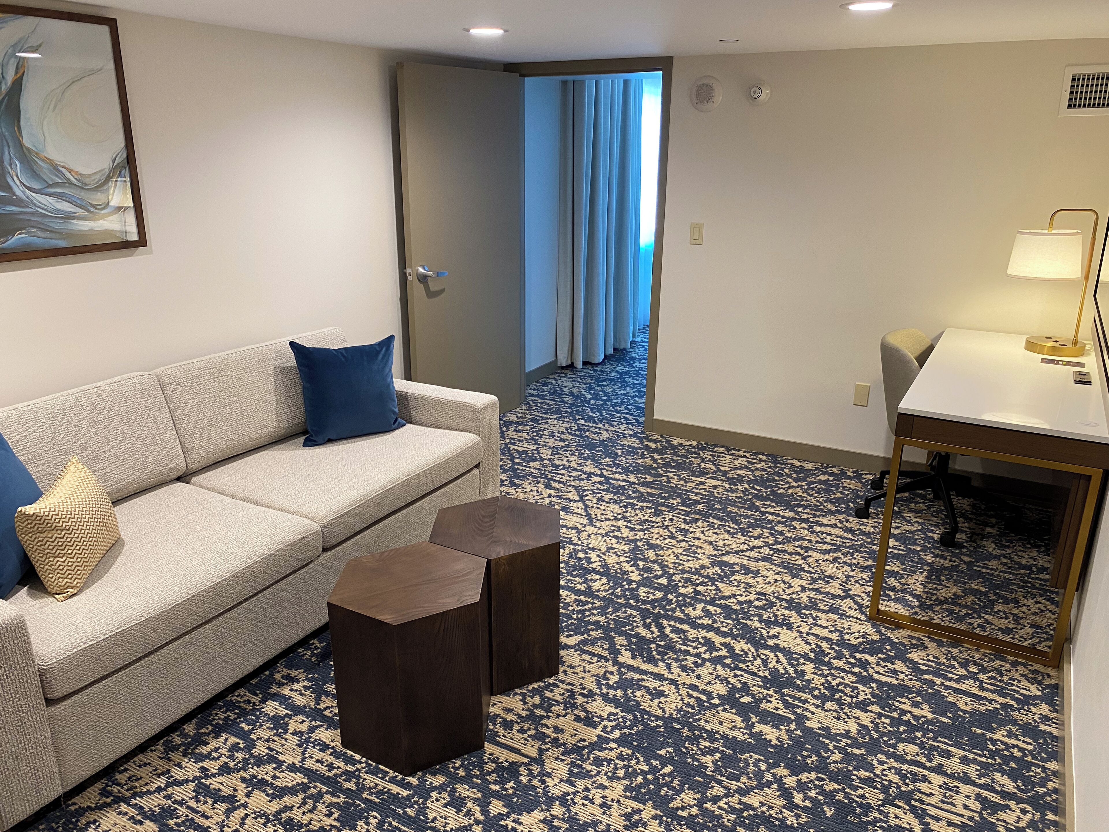A hotel room with a sofa, two side tables, a desk, and a lamp.
