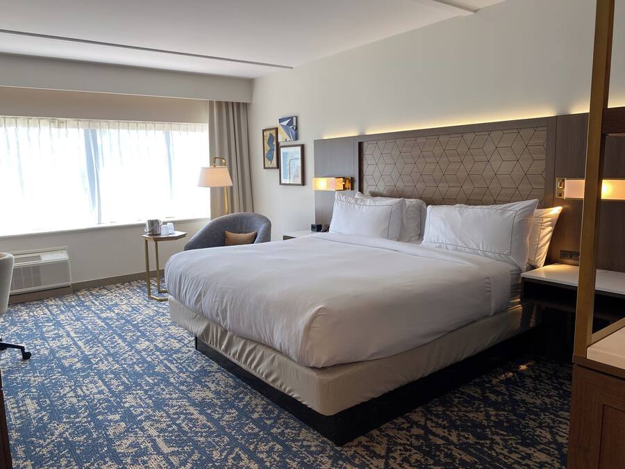 Una habitación de hotel con una cama grande, un escritorio, una silla y una ventana con cortinas.