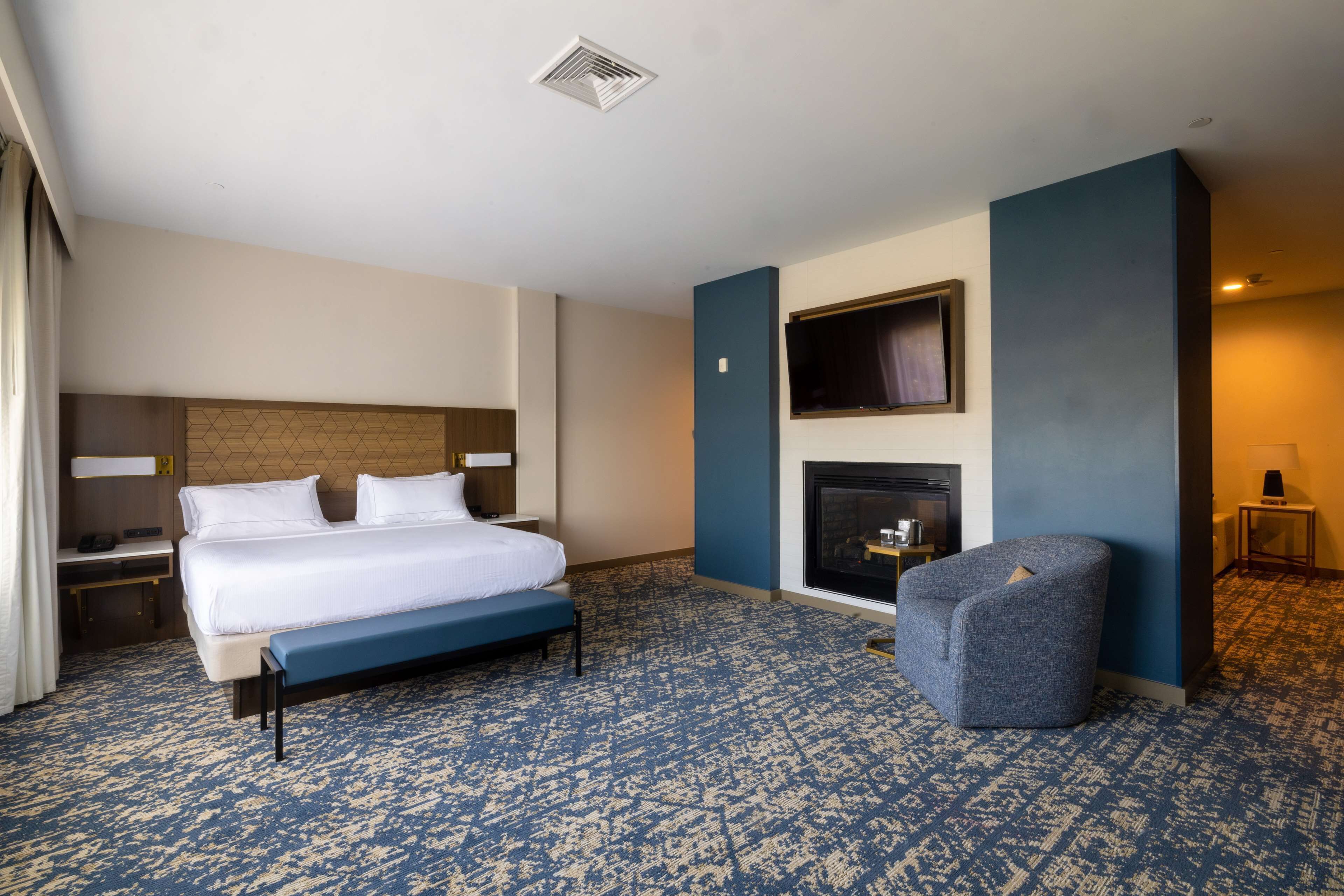 Ein Hotelzimmer mit Bett, einer Sitzbank, einem Kamin und einem Fernseher.
