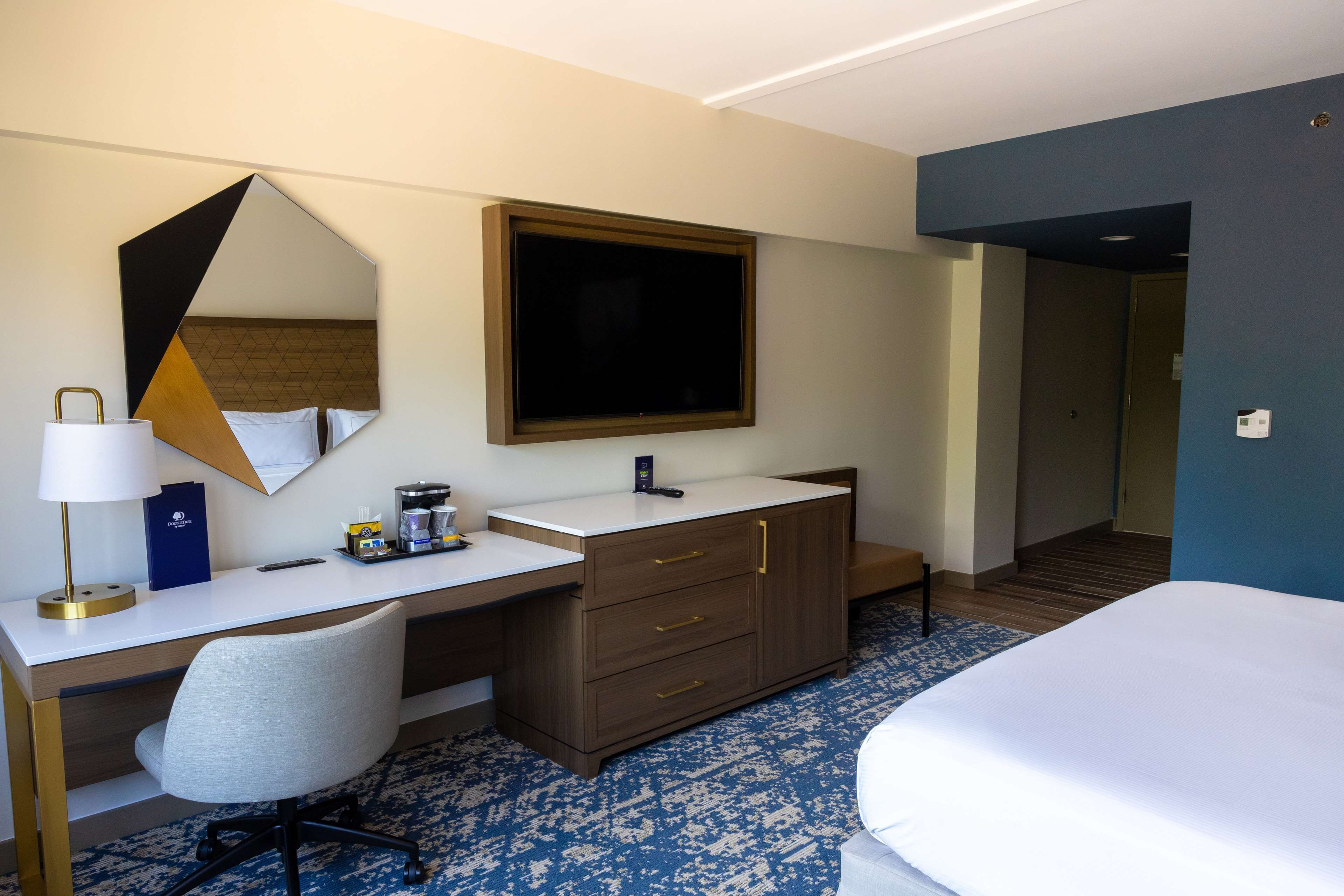 A hotel room with a bed, a desk with a mirror, a television, and a wardrobe.