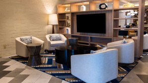 A modern living room with a large flat-screen TV, two white armchairs, a coffee table, and a patterned rug. - DoubleTree by Hilton Tinton Falls - Eatontown (Tinton Falls)