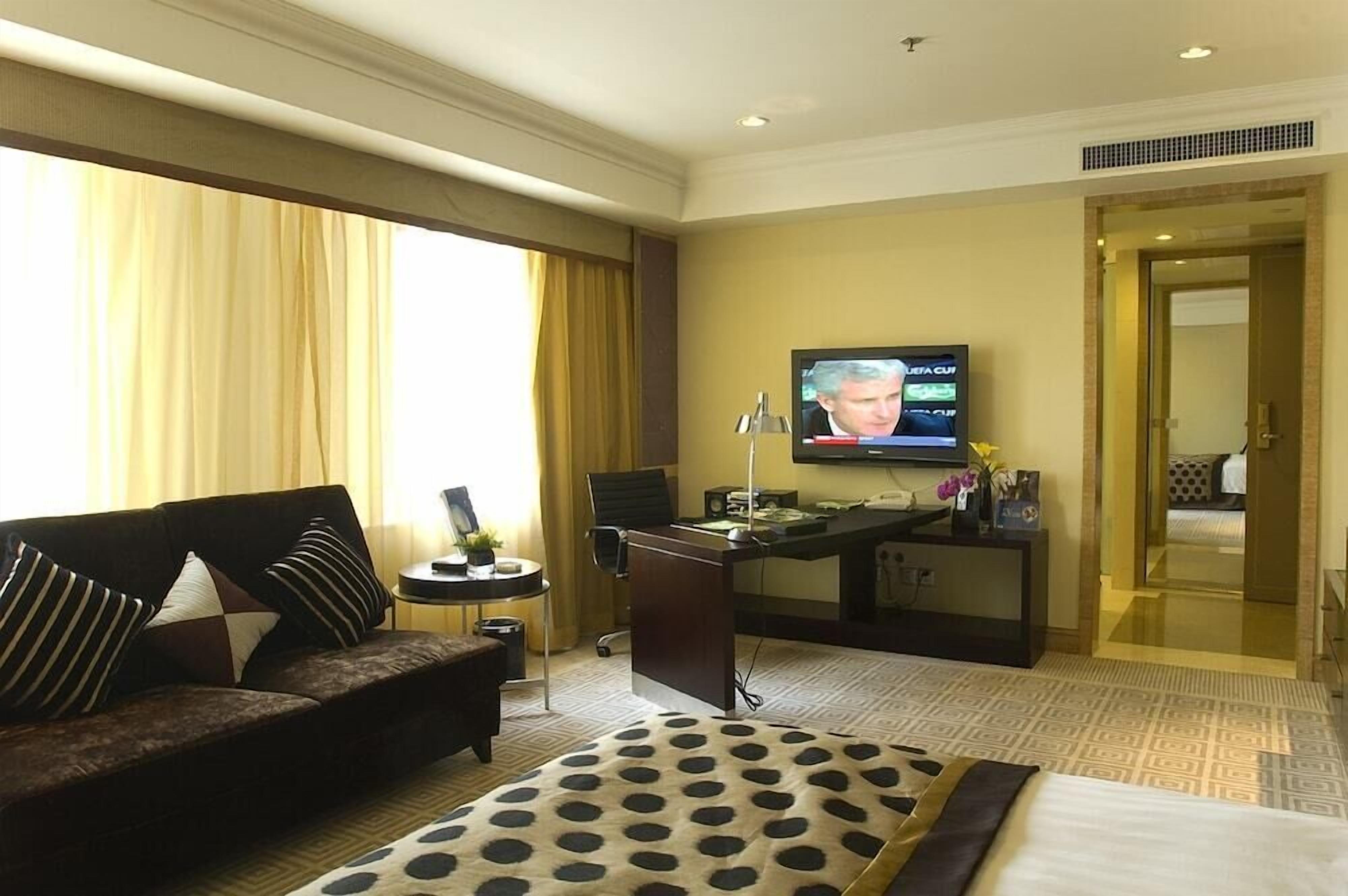 Ein Hotelzimmer mit einer Couch, einem Schreibtisch mit Computer, einem Fernseher und einem Bett.