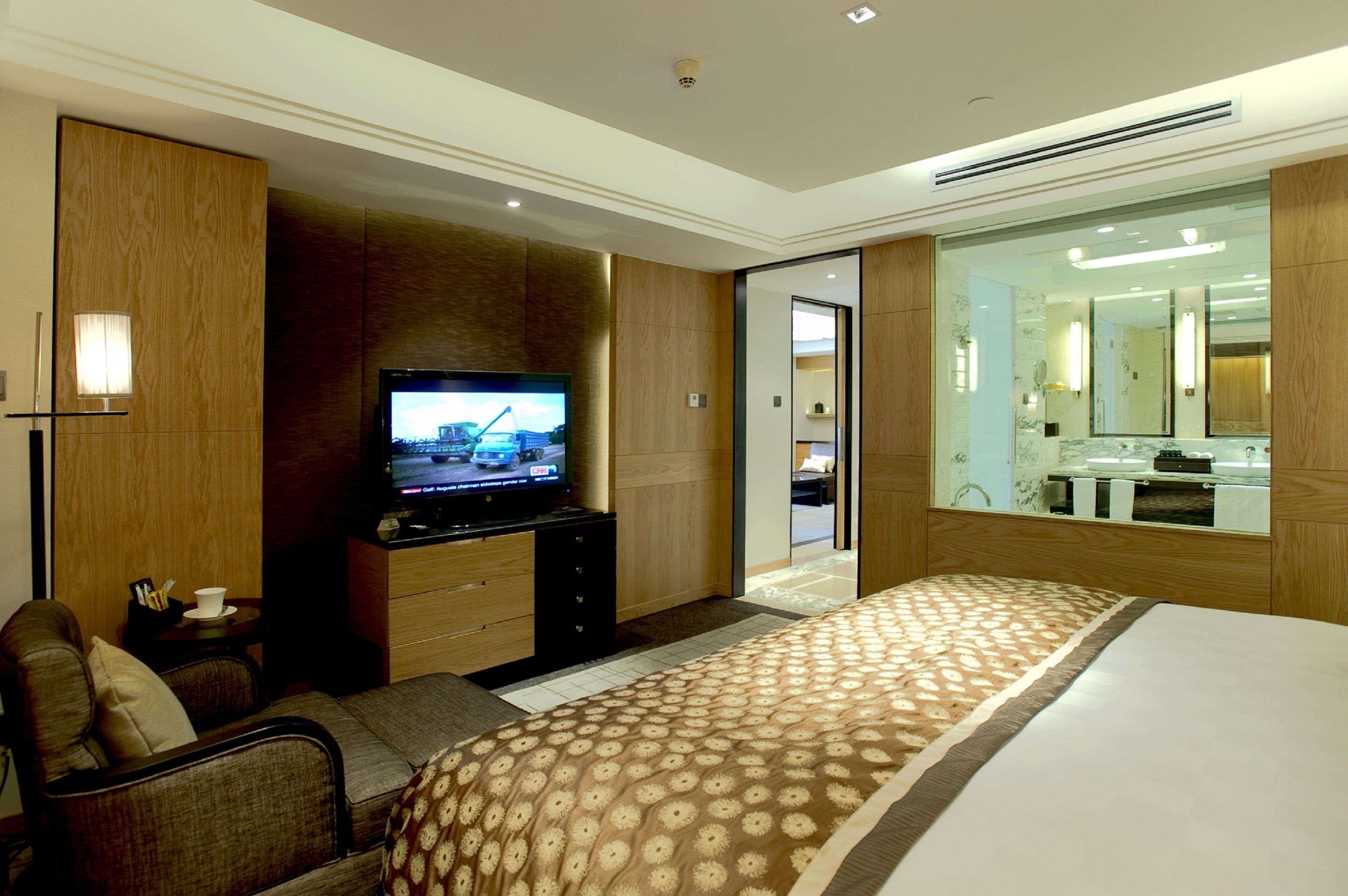 A hotel room with a large bed, a TV on a wooden cabinet, a small seating area, and a bathroom with a large mirror.
