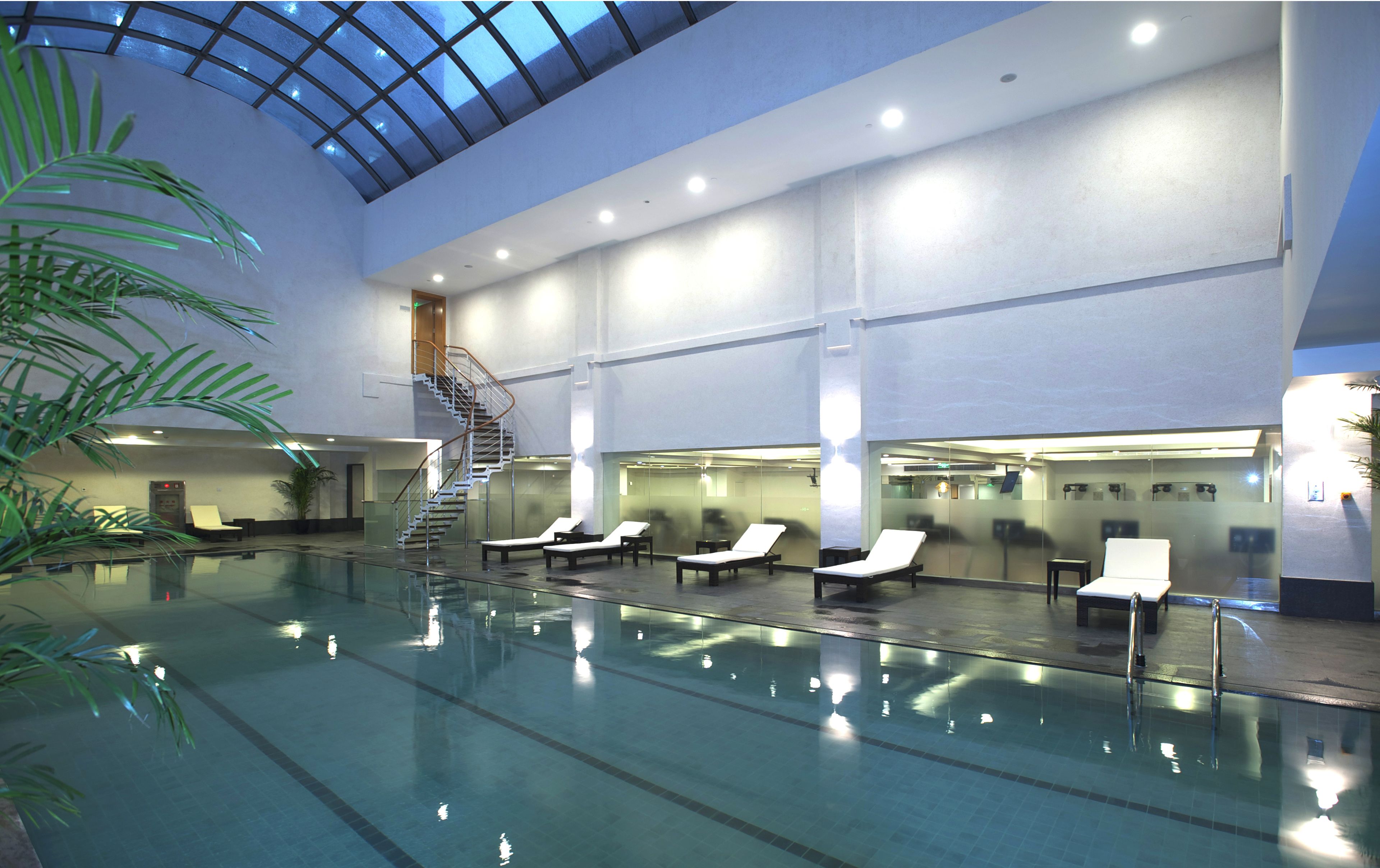 Una piscina interior con techo de cristal, múltiples sillones de descanso y una escalera.