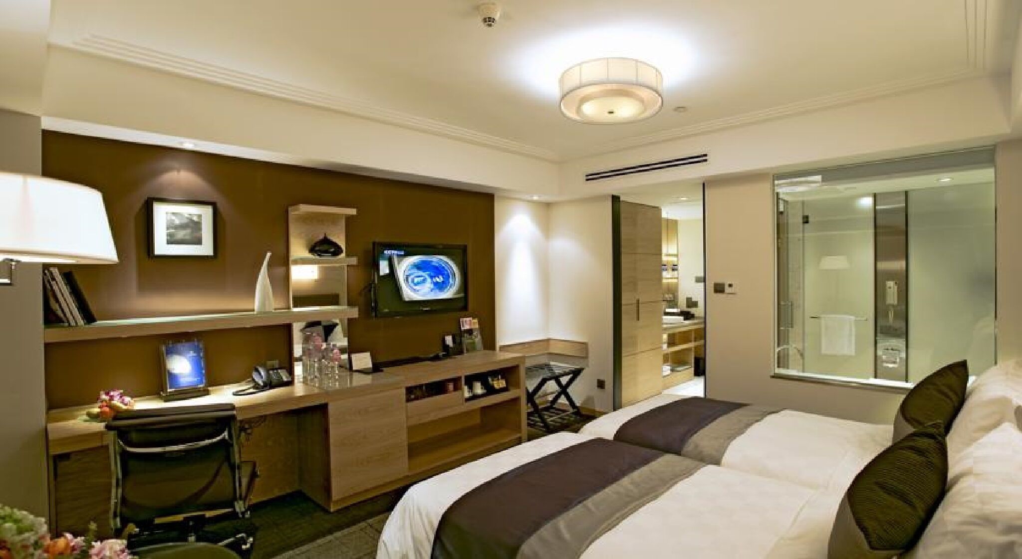 Une chambre d’hôtel équipée d’un lit, d’un bureau, d’une télévision et d’une salle de bain avec une douche en verre.