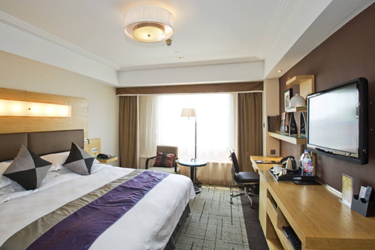 A hotel room with a large bed, a desk with a computer, a television, and a window with curtains.
