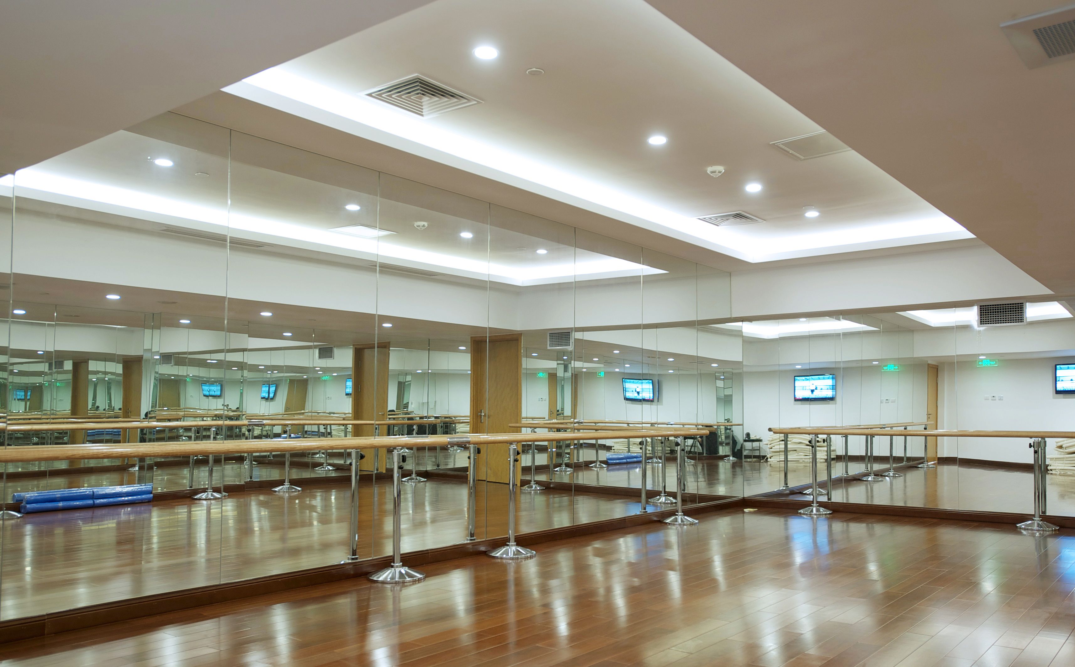 A spacious dance studio with wooden floors, mirrors, ballet barres, and ceiling lights.