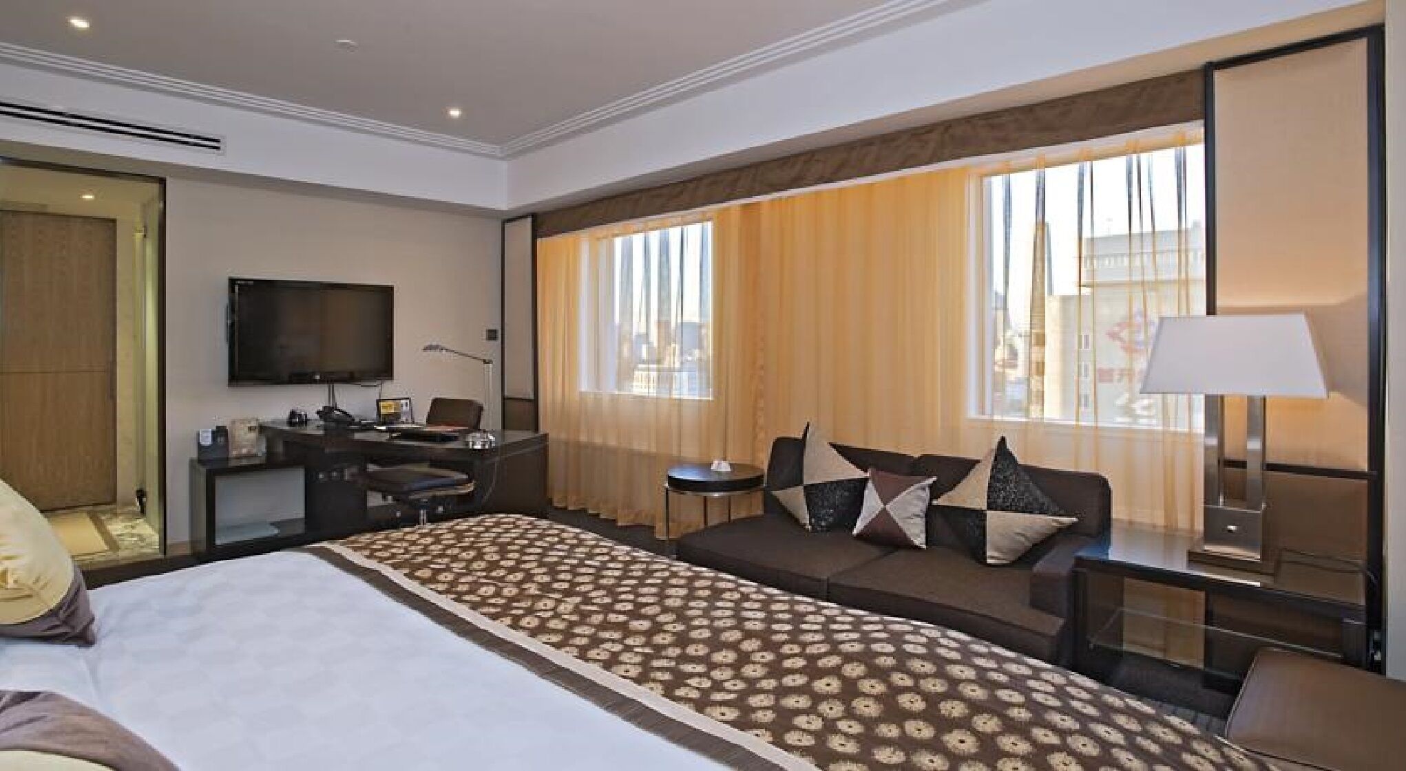 A hotel room with a large bed, a desk with a computer, a TV, and a sofa with pillows.