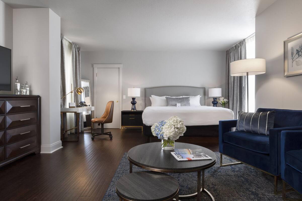 A hotel room with a bed, a desk, a chair, a sofa, a coffee table, and a TV.