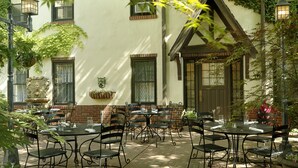 An outdoor patio with multiple tables and chairs, surrounded by a building with a white facade and brick accents. - Seven Gables, St. Louis West, a Tribute Portfolio Hotel (St. Louis)