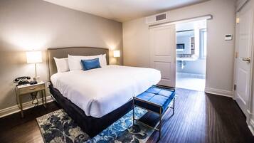 A hotel room with a large bed, bedside lamps, a small table, a bench, and a view of the outside.