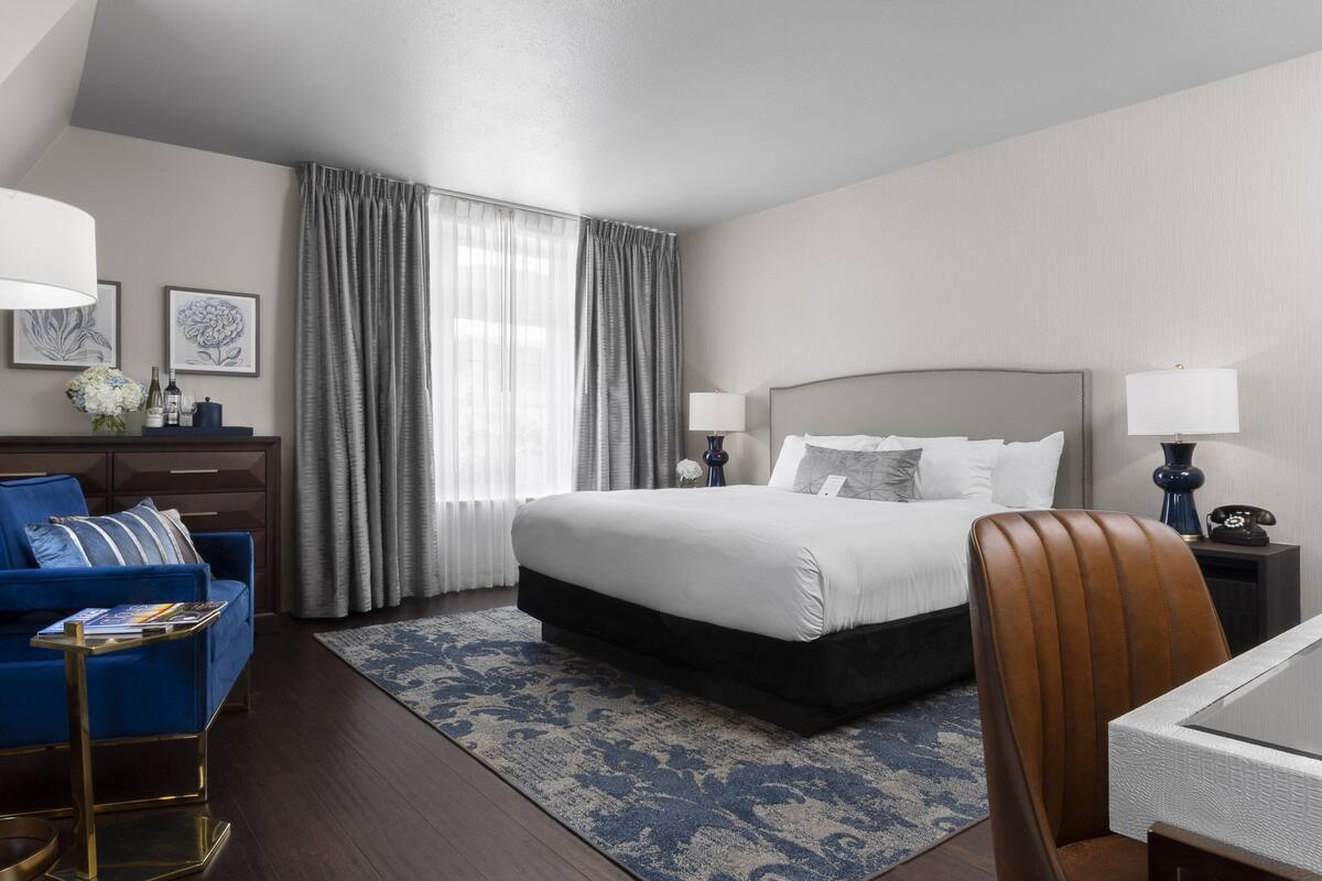 A hotel room with a large bed, a blue sofa, a desk, and a chair.