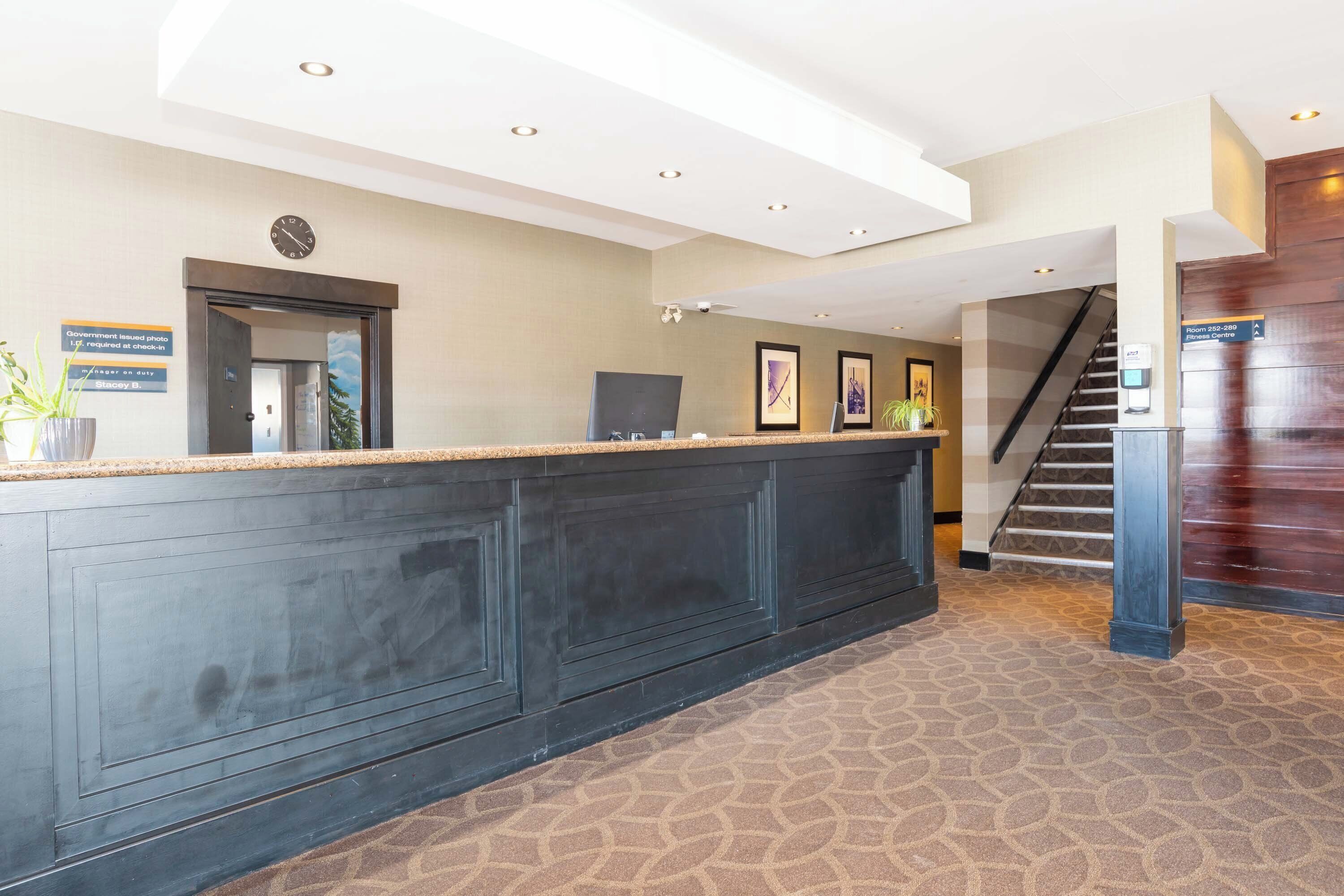 A reception area with a dark wooden reception desk, a clock, framed artwork, and a staircase leading to another floor.