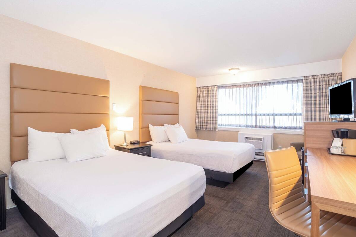 A hotel room with two beds, a desk, a chair, a television, and a window with curtains.
