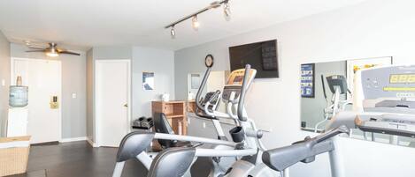A home gym with exercise equipment, a water dispenser, and a clock on the wall.