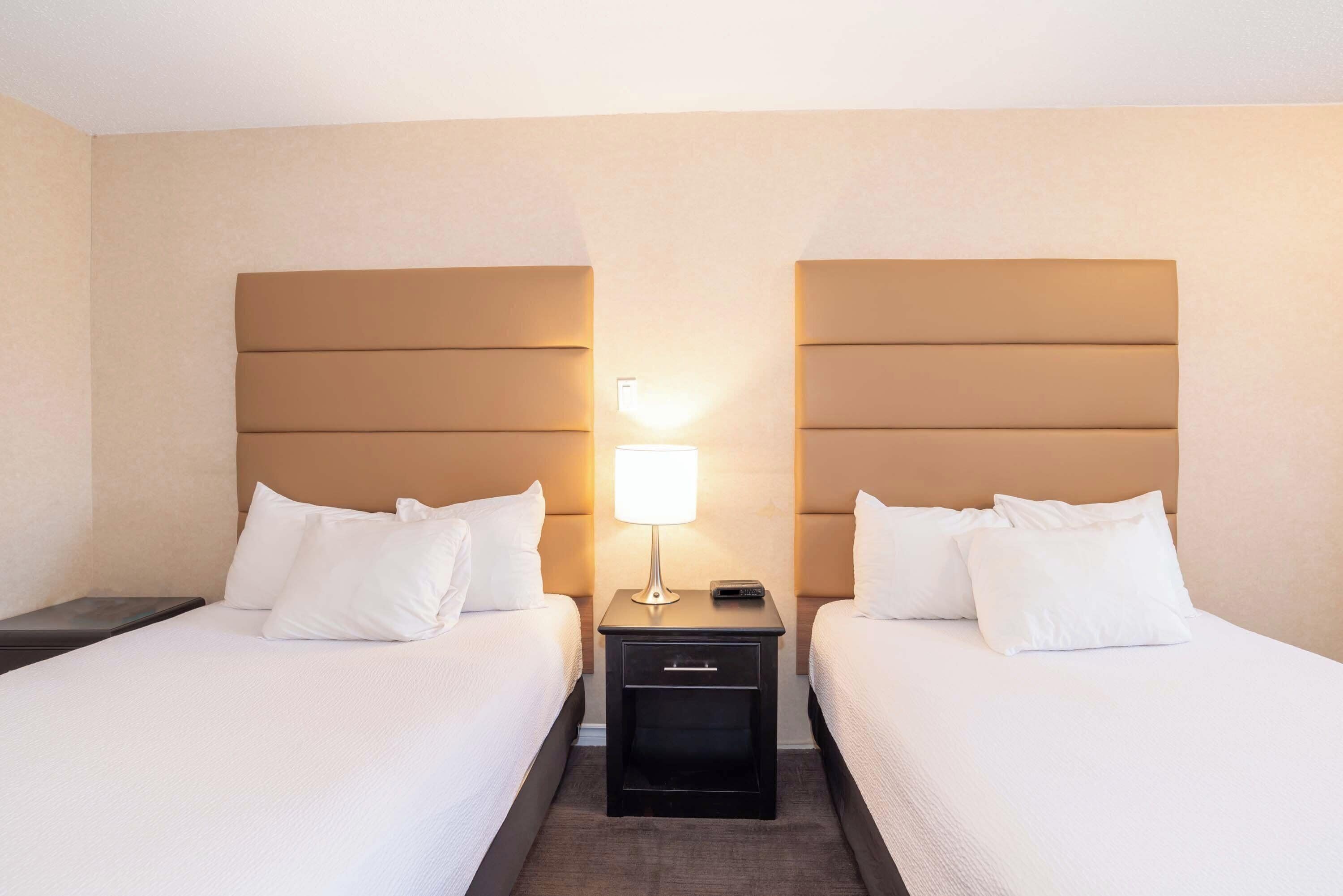 Une chambre d’hôtel avec deux lits, chacun doté de draps et d’oreillers blancs, une table de chevet avec une lampe et un petit tiroir.