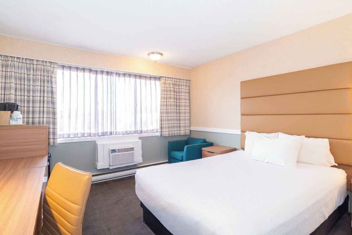 A hotel room with a bed, a desk, a chair, a small table, and a window with curtains.