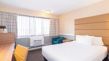 Habitación de hotel con cama, escritorio, silla, mesita y ventana con cortinas.