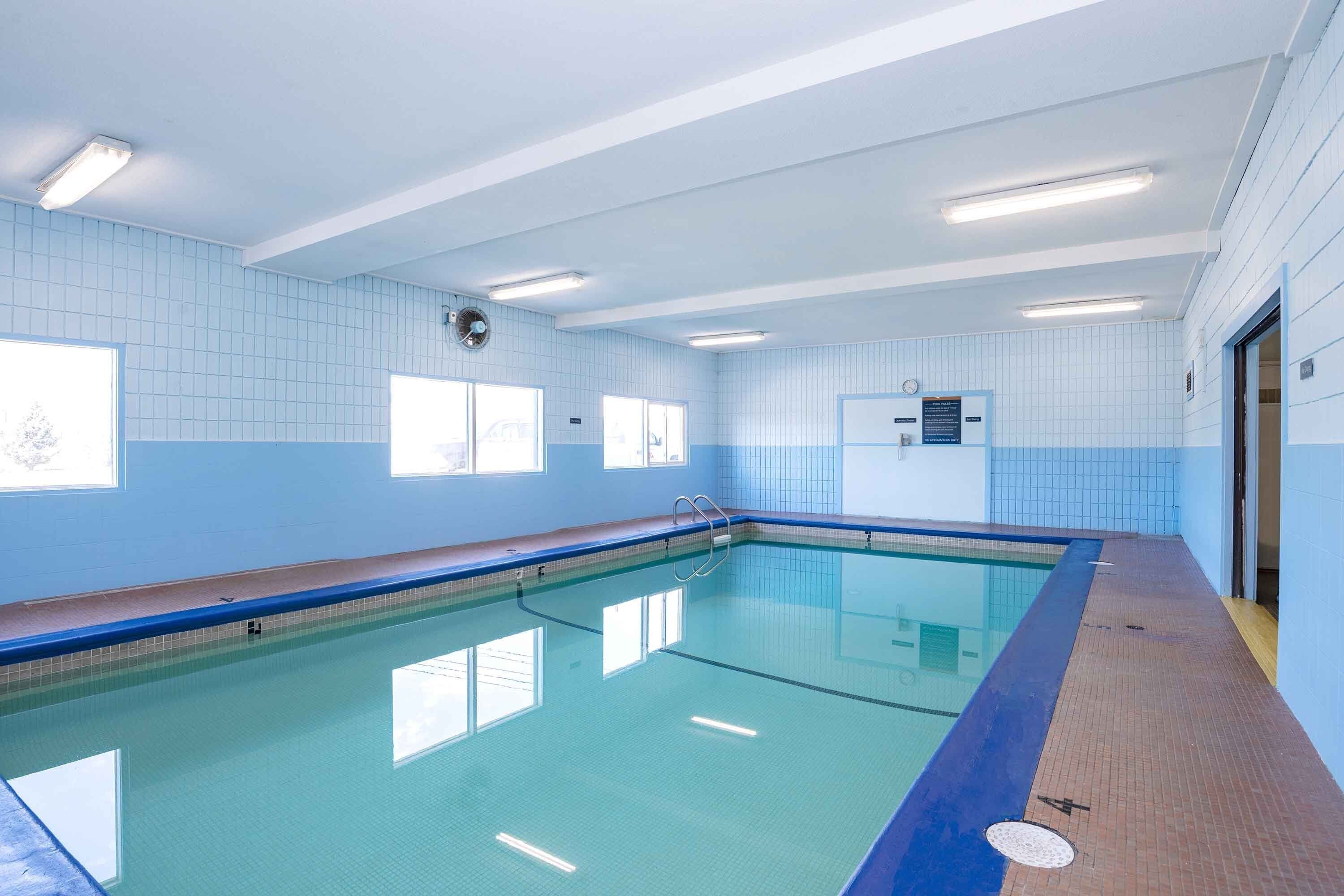 An indoor swimming pool with clear blue tiles, a wooden deck, and a blue-tiled wall.