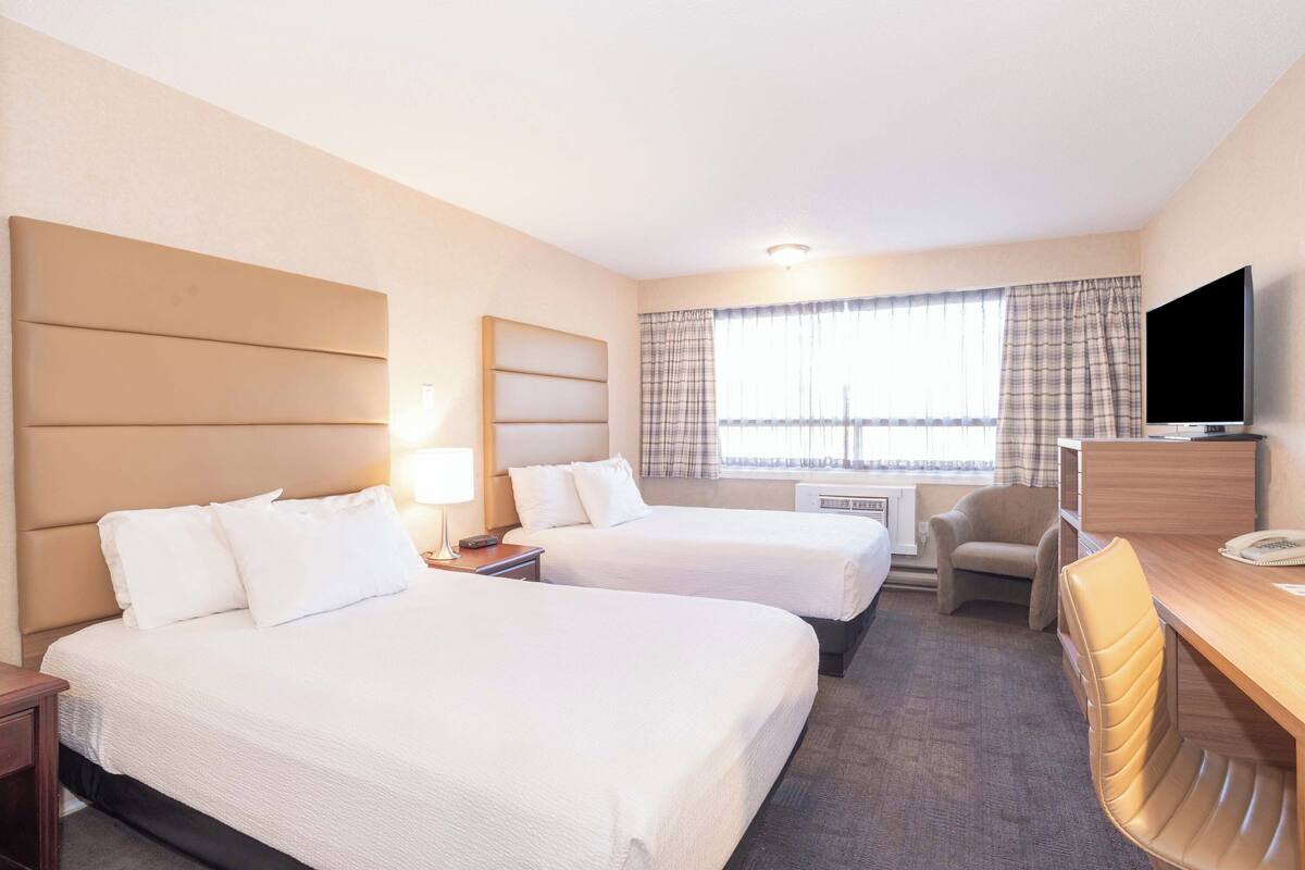 A hotel room with two beds, a desk, a chair, a television, and a window with curtains.