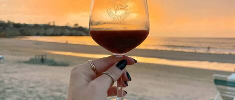 A hand holding a wine glass with a beach and sunset in the background.