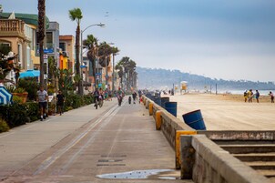 Un paseo marítimo con edificios, palmeras y una playa al fondo.