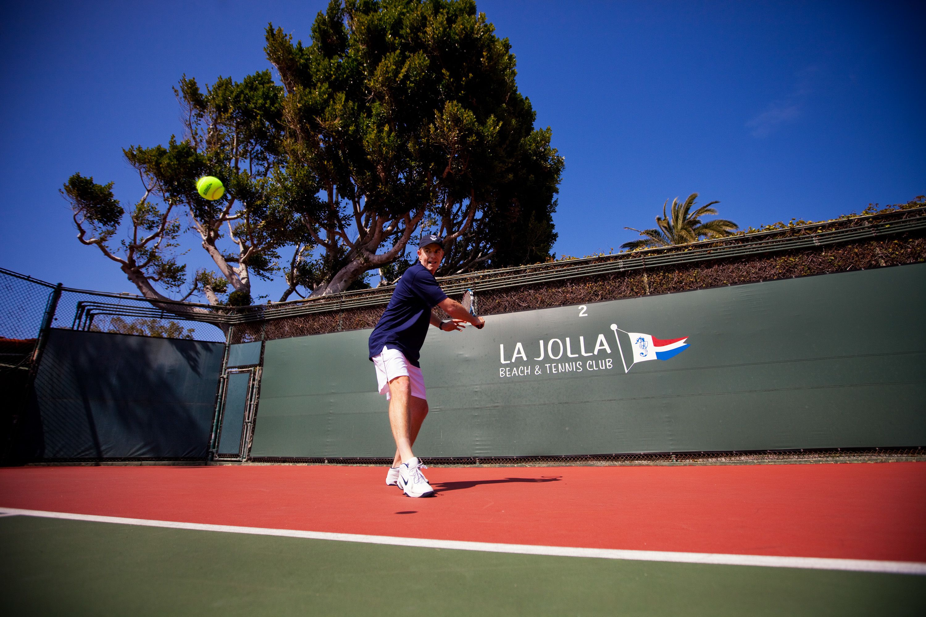 A tennis court with a net, a player in mid-action, and a banner with "LA JOLLA BEACH & TENNIS CLUB" text.