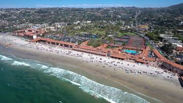 An aerial view of a coastal area with a beach, a parking lot, and a sports complex.