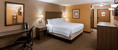 A hotel room with a bed, desk, chair, and a mirror.