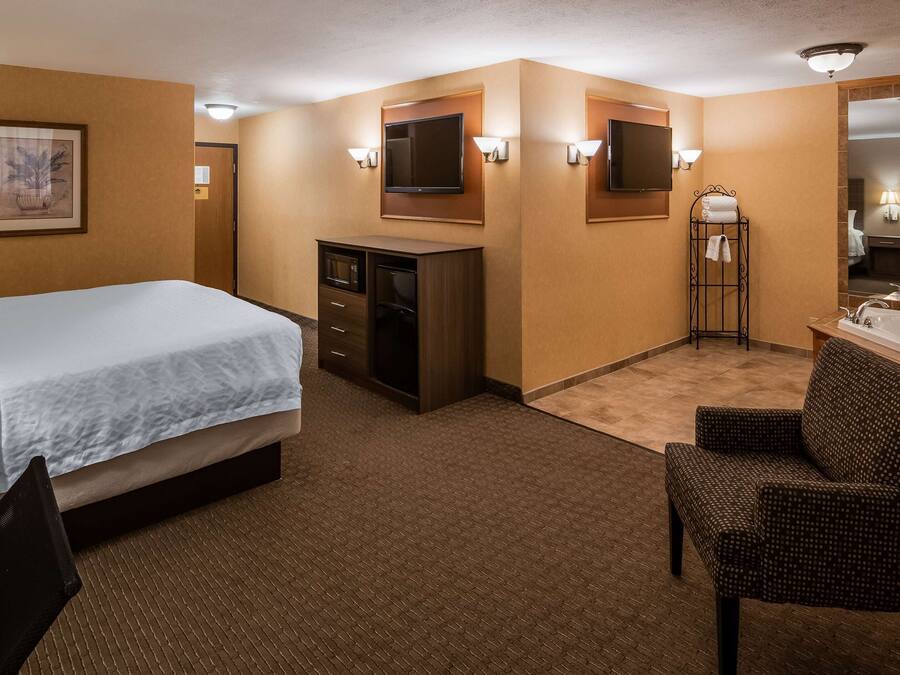 A hotel room with a bed, a desk, a chair, a TV, and a bathroom with a bathtub and sink.