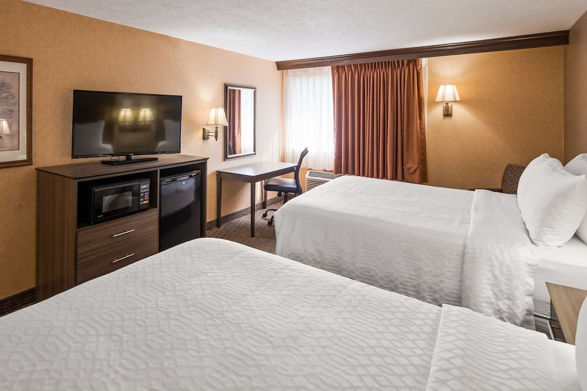 A hotel room with two beds, a desk, a television, a microwave, and a framed picture on the wall.