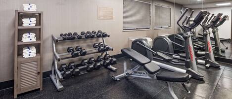 Un gimnasio con equipo de ejercicio, un reloj y un cartel con normas de seguridad.