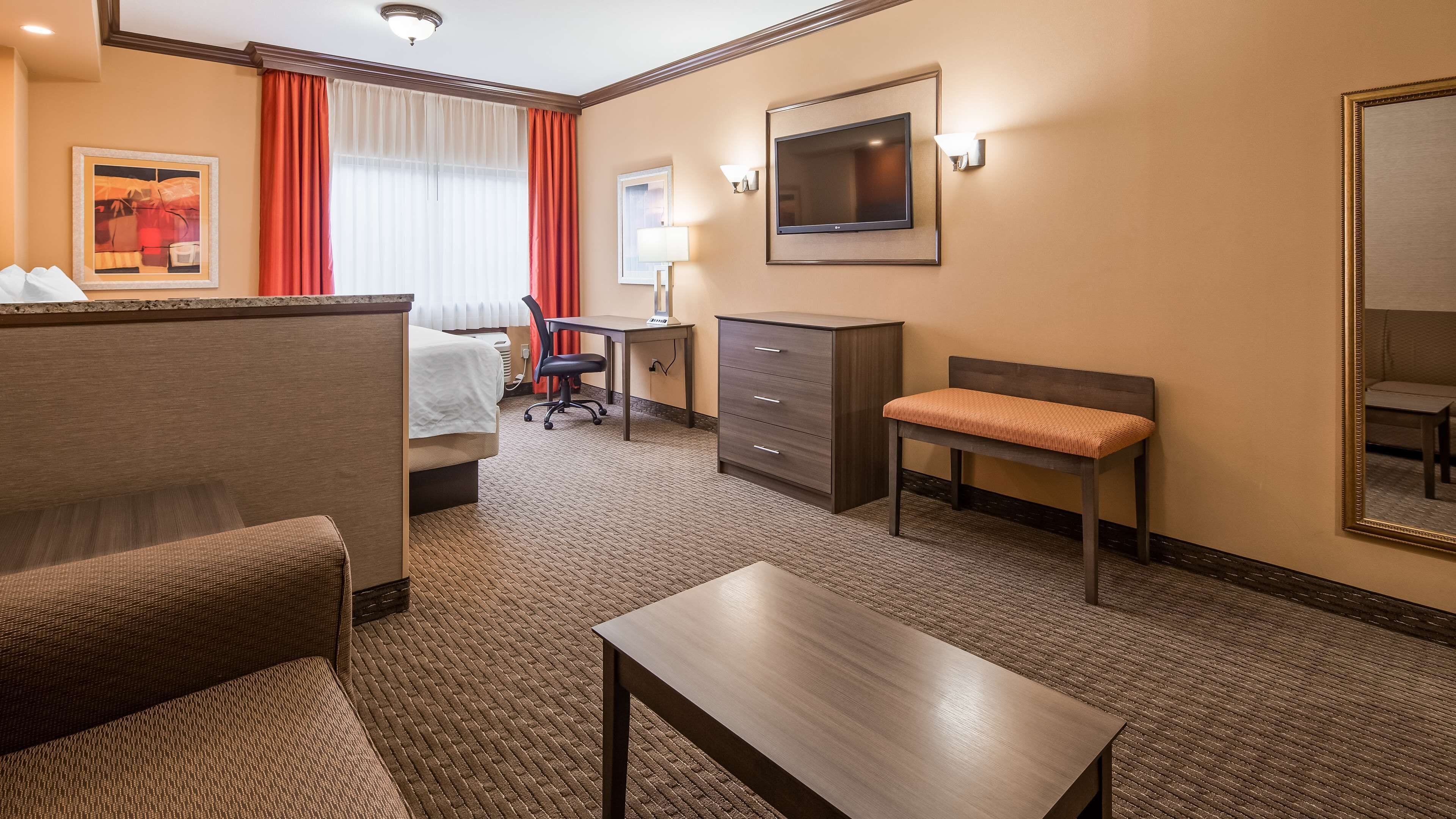A hotel room with a bed, a desk, a chair, a dresser, a TV, and a mirror.
