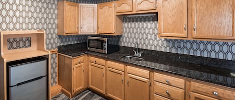 A compact kitchen with wooden cabinets, a built-in microwave, and a stainless steel refrigerator.