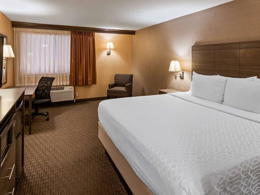 A hotel room with a large bed, a desk with a television, a chair, and two wall-mounted lamps.