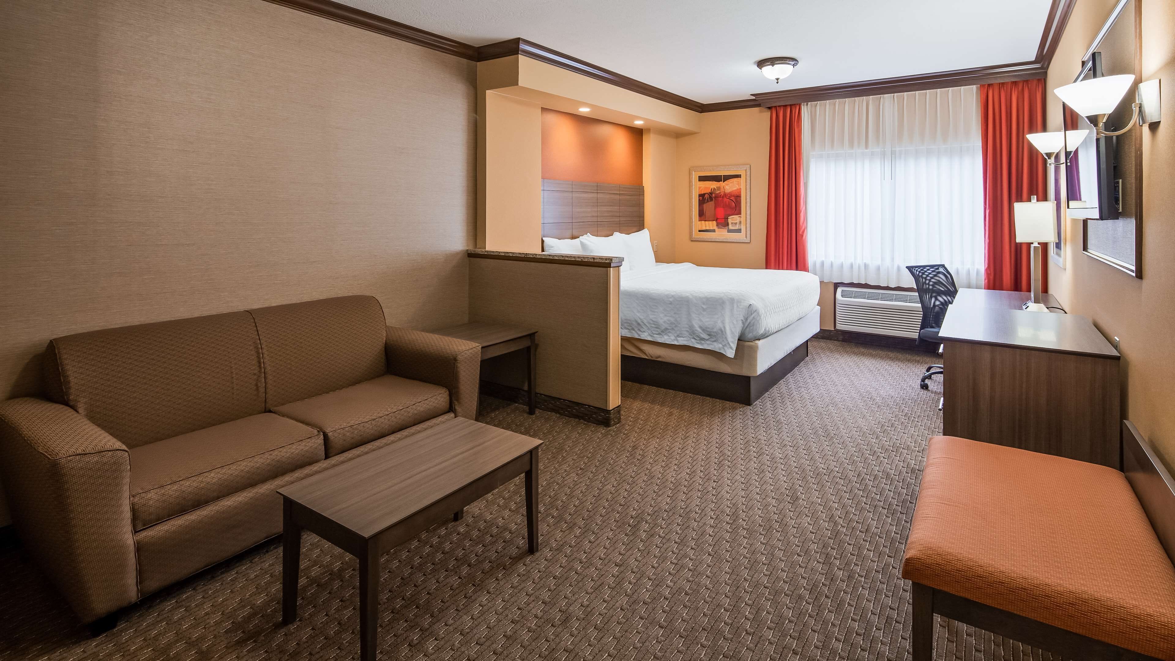 Habitación de hotel con sofá, una mesita, cama con cabecera, escritorio y una silla.