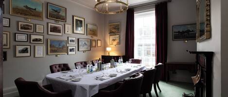 A dining room with a long table set for a meal, framed pictures on the walls, and a chandelier.