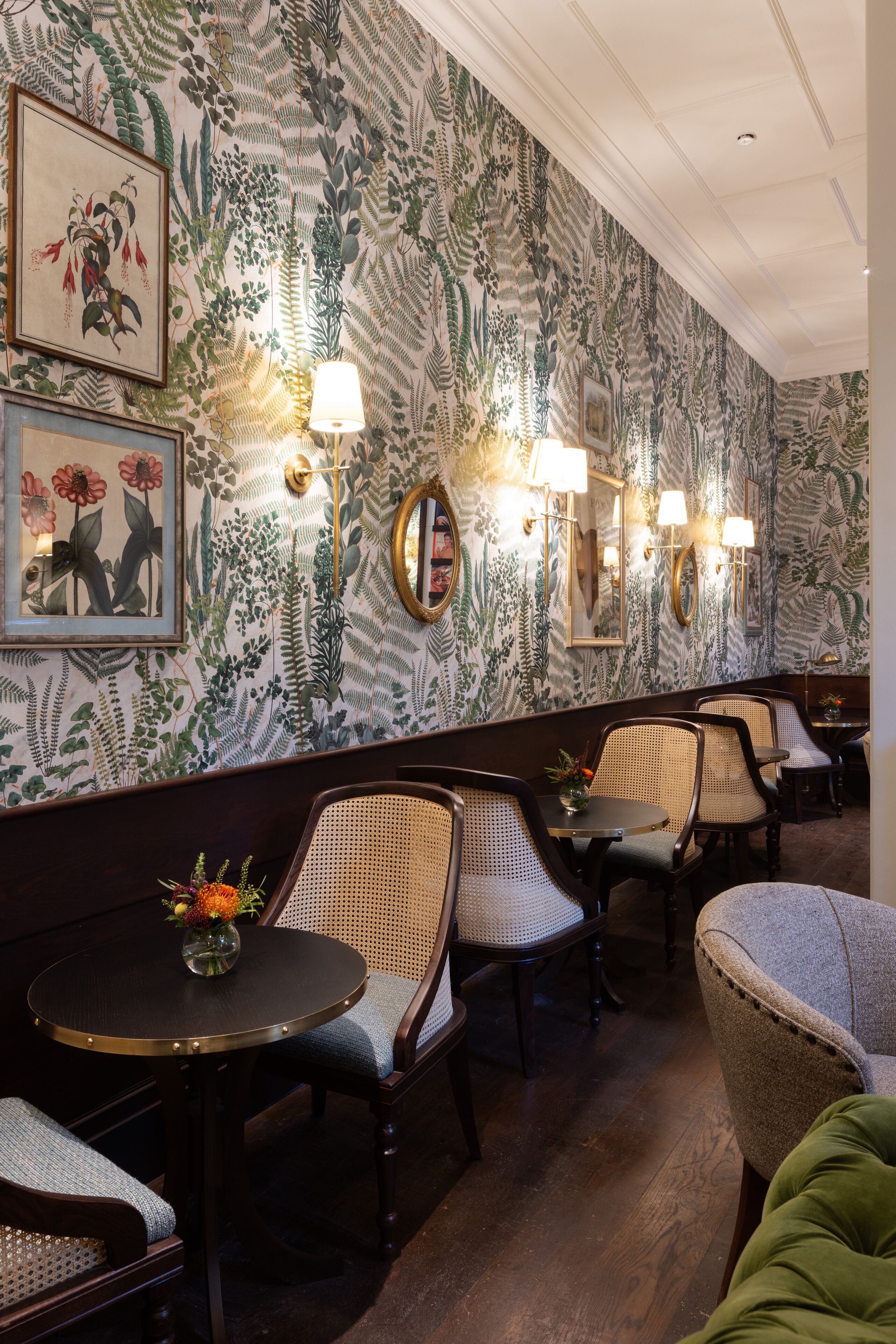 Ein Restaurant mit gemustertem Wandpapier, Korbstühlen und Tischleuchten.